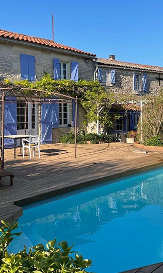 Gîte de Charme avec Piscine et Volets Bleus en France Maison de campagne en pierre avec piscine, terrasse et volets bleus sous un ciel d'été dégagé.